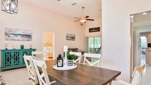 A dining area with a wooden table, white chairs, a teal cabinet, and a ceiling fan. - Charming 3-bedroom house in Palm Coast: Near Beach (Palm Coast)
