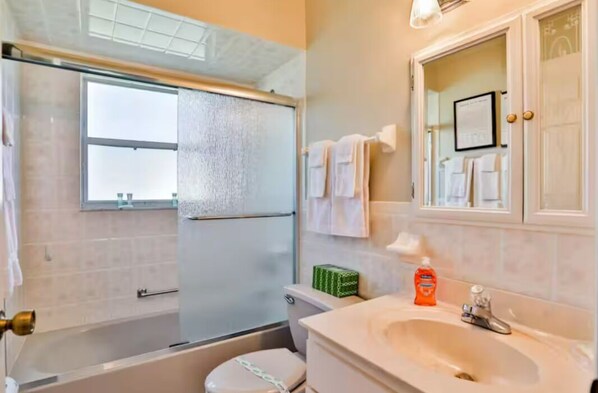 A bathroom with a glass shower enclosure, a toilet, a sink with a mirror, and towels on the wall.