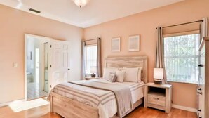 A bedroom with a large bed, bedside tables, a window with curtains, and a door leading to another room. - Charming 3-bedroom house in Palm Coast: Near Beach (Palm Coast)