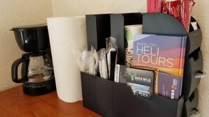A black storage box containing travel brochures, a coffee maker, and a roll of paper towels on a wooden table.