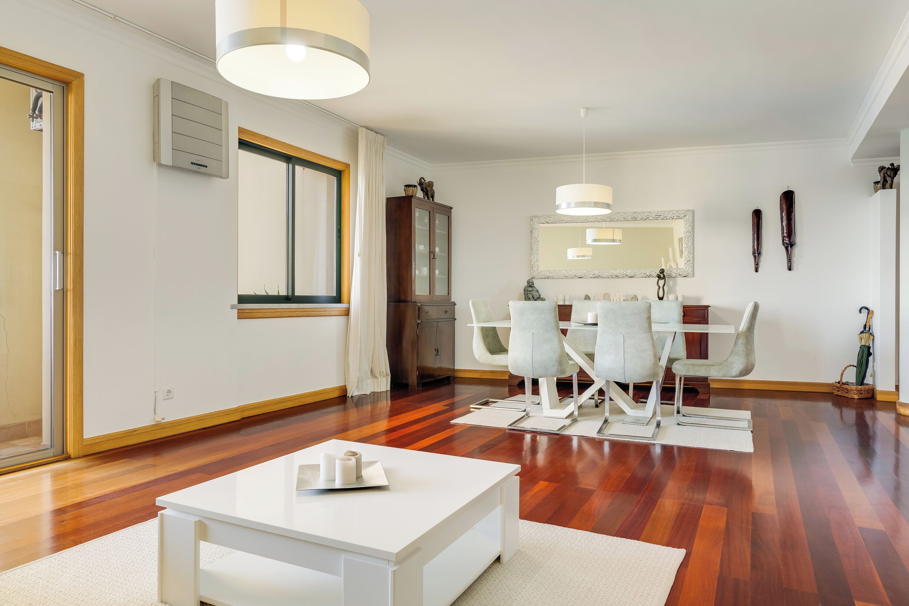 A modern living room with a dining area, wooden flooring, a white coffee table, and a dining table with chairs.