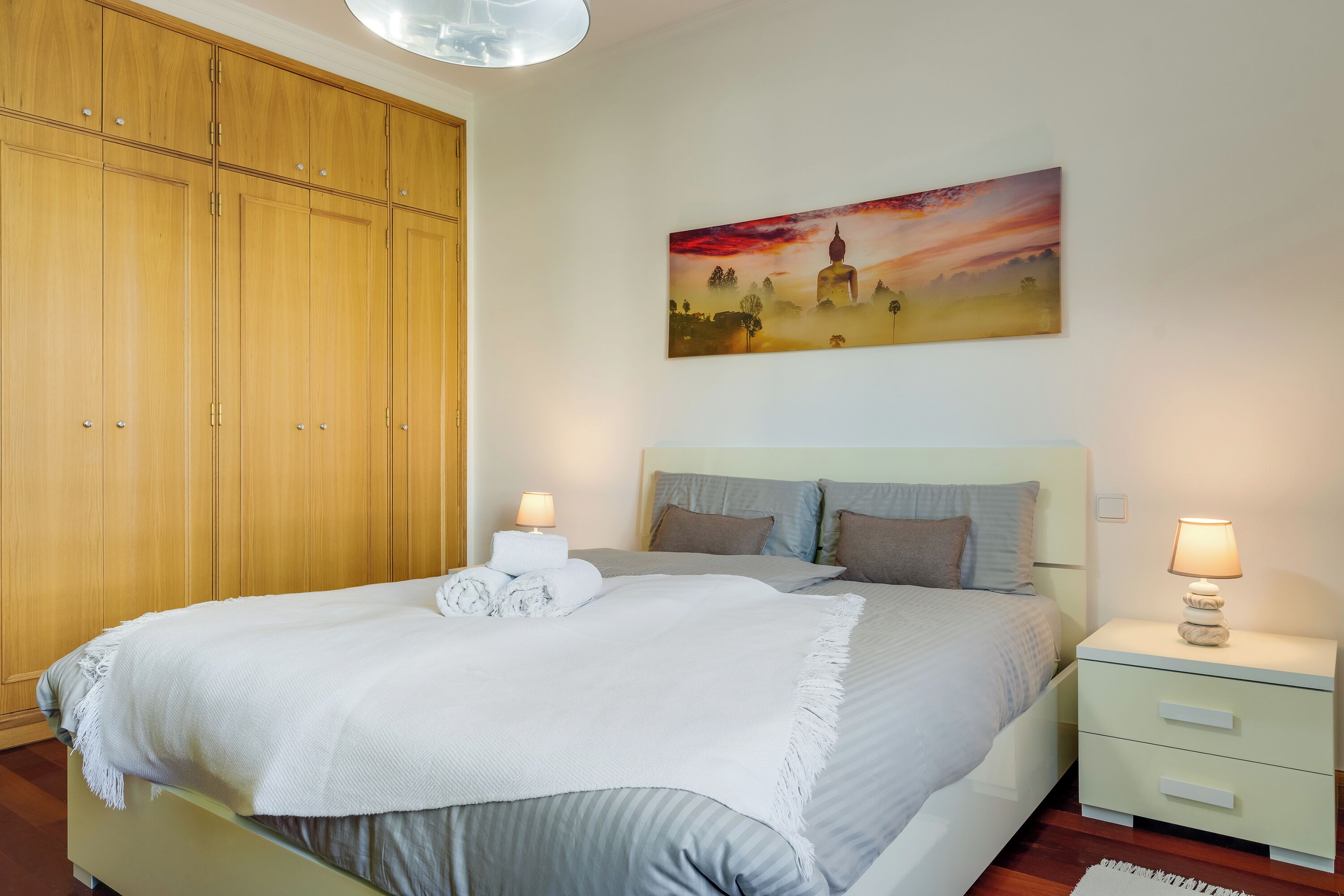Een slaapkamer met een bed, nachtkastjes, een schilderij en een kledingkast.