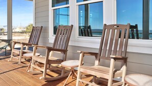 A wooden rocking chair and a table on a wooden deck with large windows. - Windchimes (Port St. Joe)