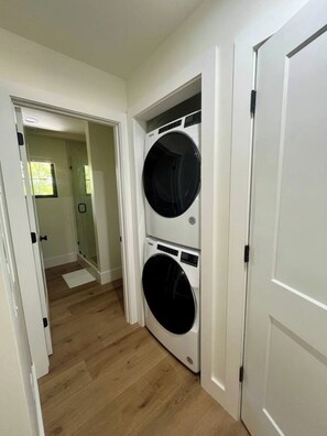 A laundry room with two stacked front-loading washing machines, wooden flooring, and white walls.