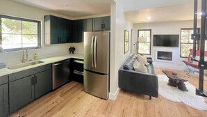 Une cuisine moderne avec des meubles de couleur sombre, un réfrigérateur en acier inoxydable et un plancher en bois.