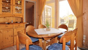 A wooden dining area with a table and chairs, a cabinet with glass doors, and a view through large windows. - Ferienhaus im Ferienpark Mueritz (Rechlin)