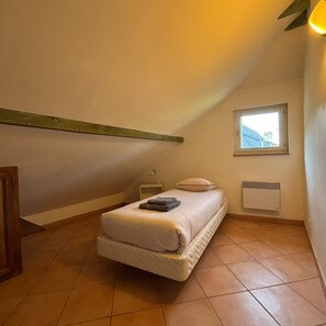 A small, single-bed room with a sloped ceiling, a window, a radiator, and a bedside table.