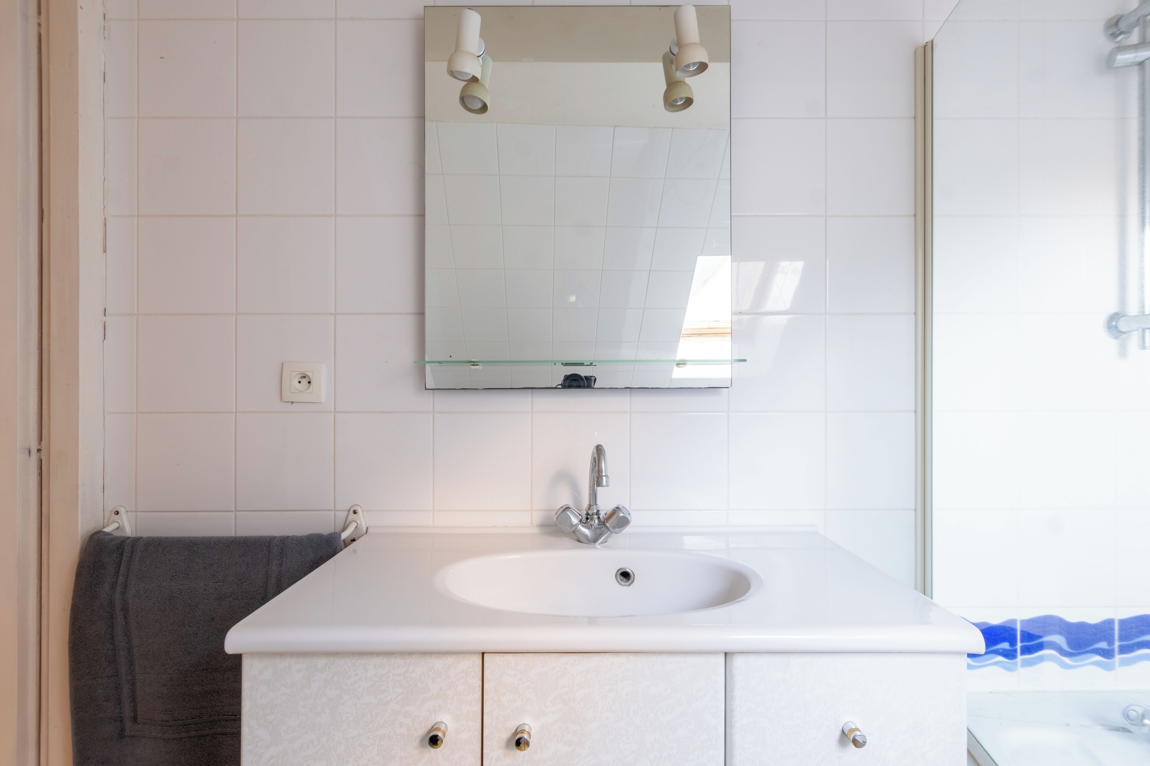 A bathroom with a white sink, a mirror, and a towel hanging on the wall.