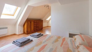 Quarto com teto inclinado, guarda-roupa de madeira, cama com roupa de cama estampada e um claraboia.