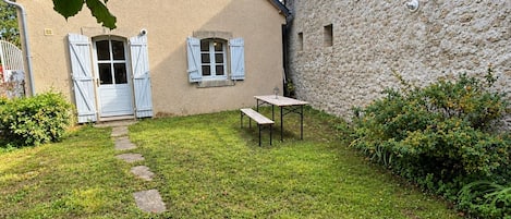 A house with a stone wall, a paved pathway, and a small table with a bench.