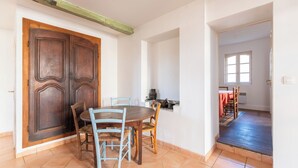 Uma sala de jantar com mesa e cadeiras de madeira, uma porta grande de madeira e uma janela ao fundo.