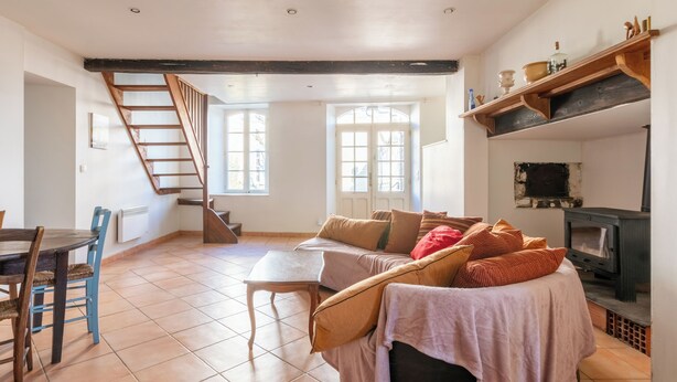 Uma sala de estar ampla com escada de madeira, lareira e área de refeições com mesa e cadeiras.