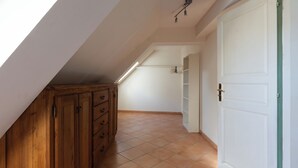 Um quarto com teto inclinado, armários de madeira, porta branca e chão de azulejos.