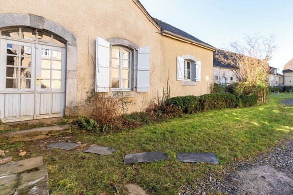 A house with a stone pathway leading to a wooden door, surrounded by a well-maintained lawn and bushes. - La Maison Vergès - 3 bedrooms - large living room - small garden (Ossun)