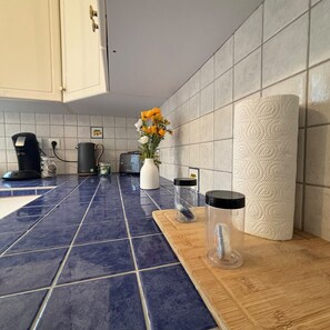 Een keuken met blauwe en witte tegels, een koffiezetapparaat, een waterkoker, een vaas met bloemen en een rol keukenpapier.