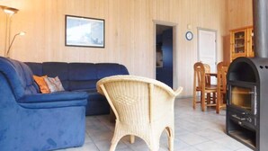 A room with a blue sofa, wicker chair, dining table, and a wood-burning stove. - Ferienhaus mit Sauna im Ferienpark Mirow (Mirow)