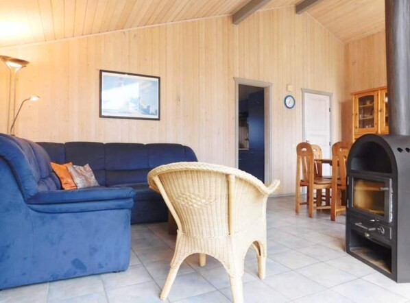 Une pièce avec un canapé bleu, un fauteuil en osier, une table à manger et un poêle à bois.