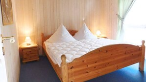 A wooden bed with a headboard, two bedside tables with lamps, and a wooden wall. - Ferienhaus mit Sauna im Ferienpark Mirow (Mirow)