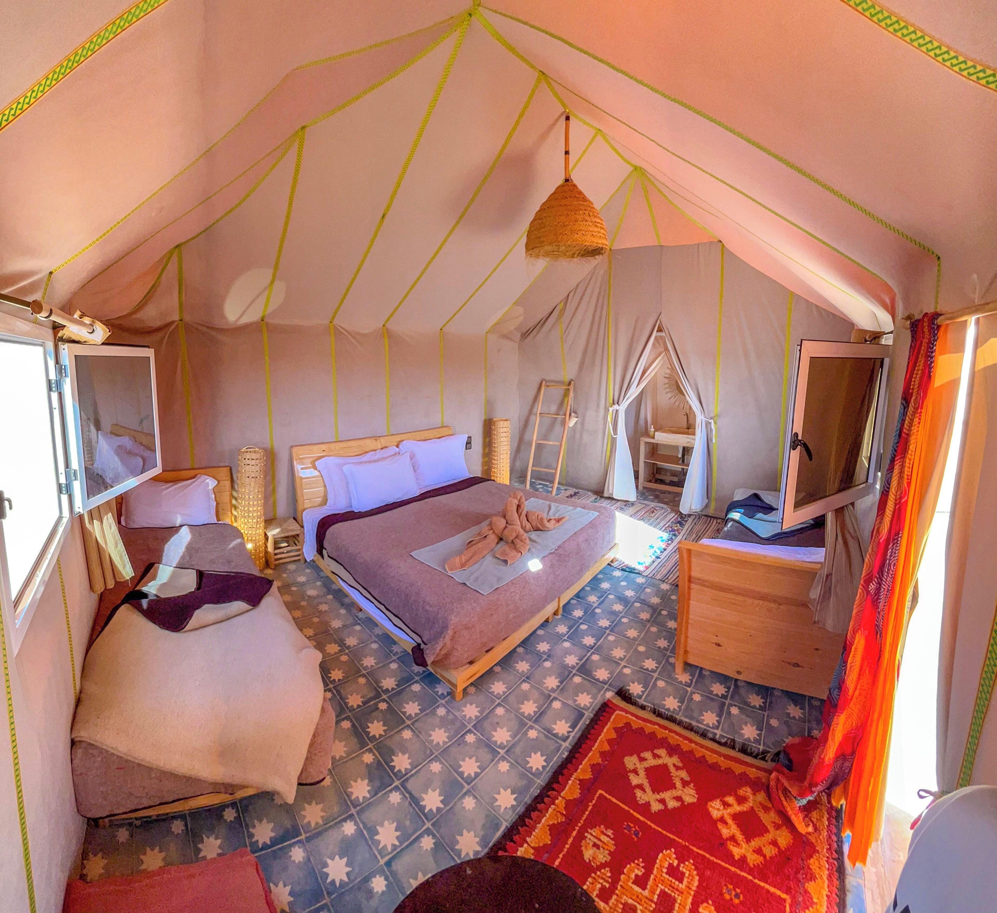 A tent with a bed, a wooden nightstand, a hanging light, and a patterned rug.
