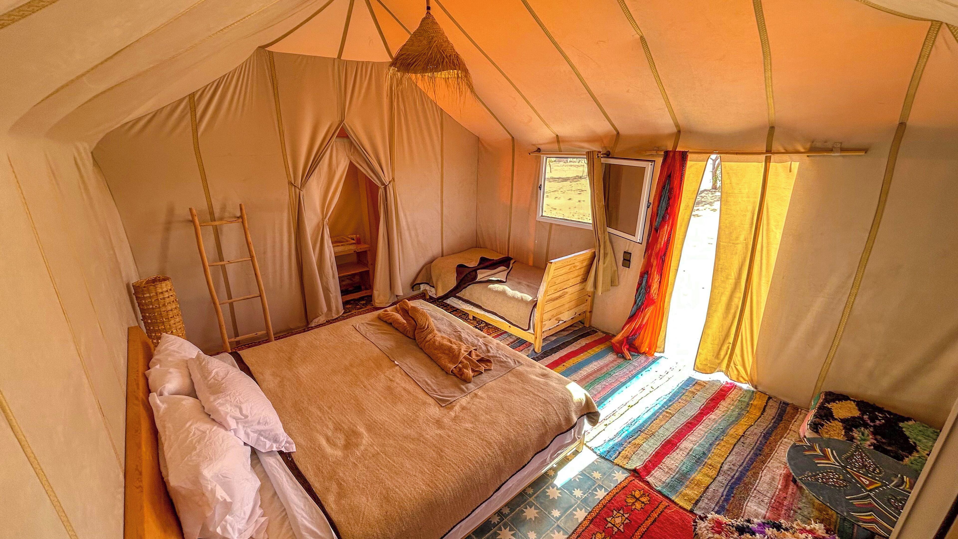 A tented room with a bed, a wooden ladder, a window, and a colorful rug.