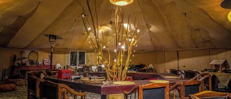 A tented room with a central table, chairs, and a hanging light fixture.