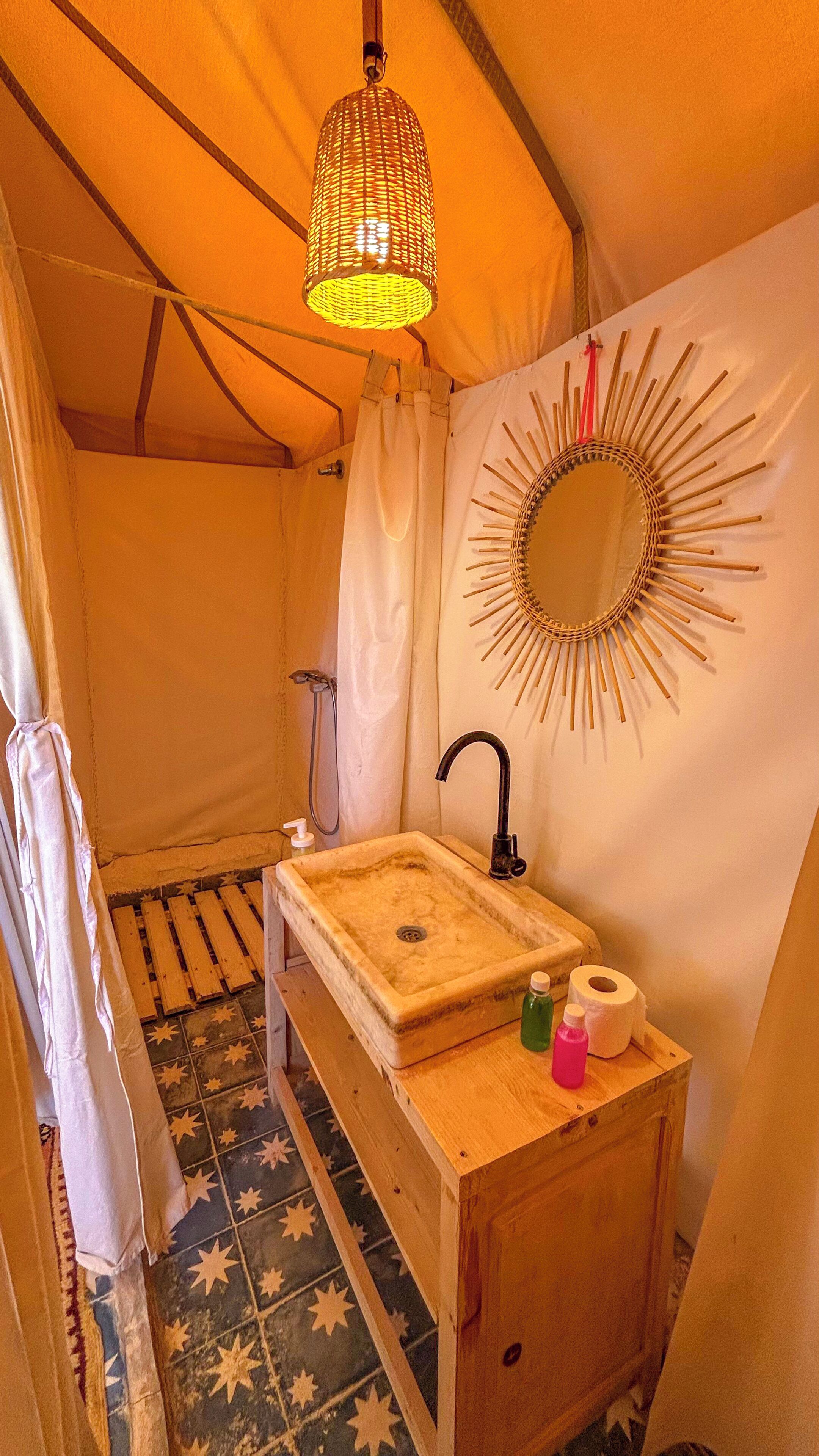 A compact, well-lit tent bathroom with a sink, mirror, and shower.