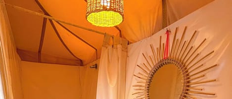 A compact, well-lit tent bathroom with a sink, mirror, and shower.