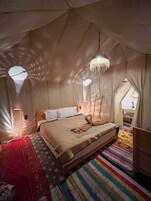 Habitación tipo tienda con cama, una lámpara colgante y un ventanal pequeño.