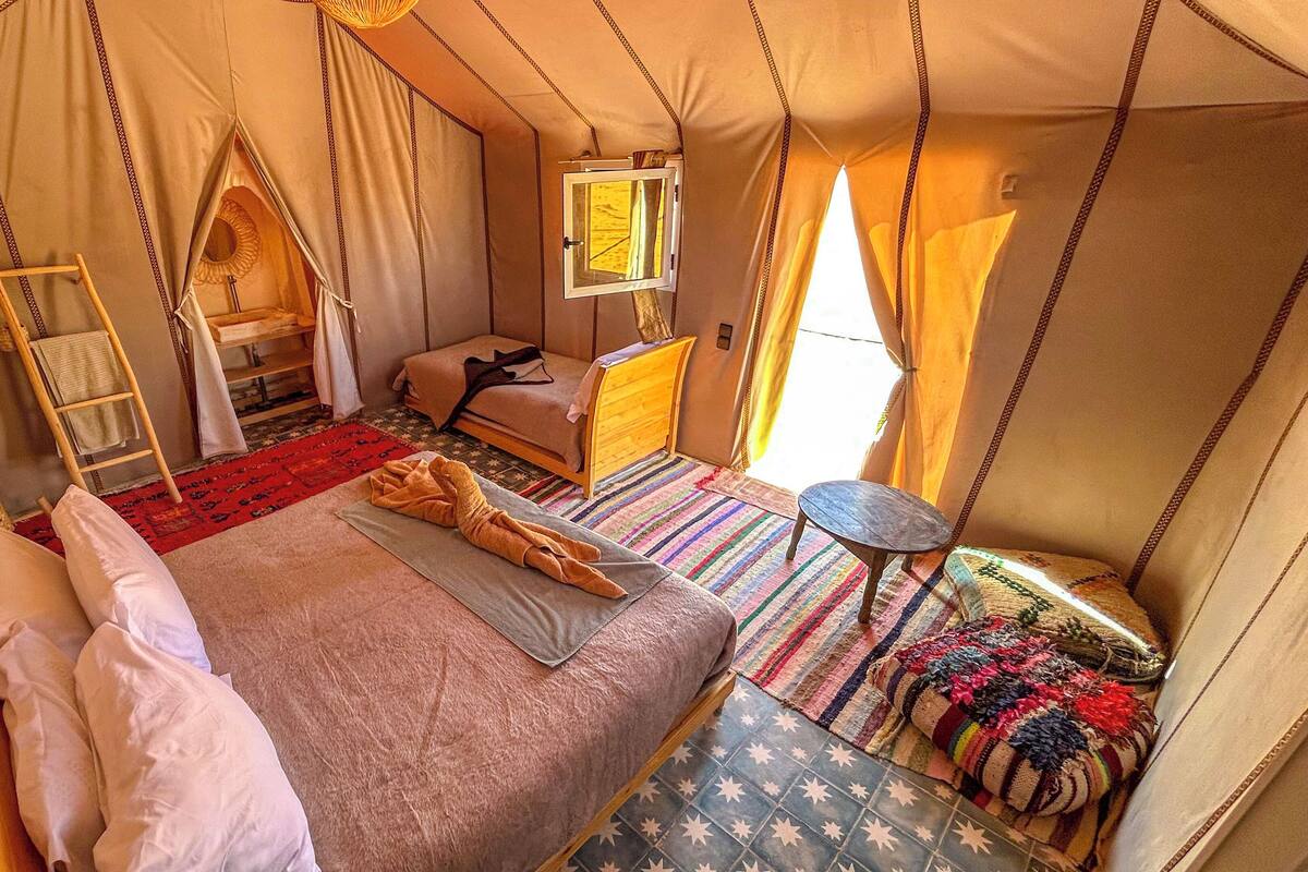 Una habitación con tienda de campaña, una cama, una mesita, una silla, una ventana y una escalera.