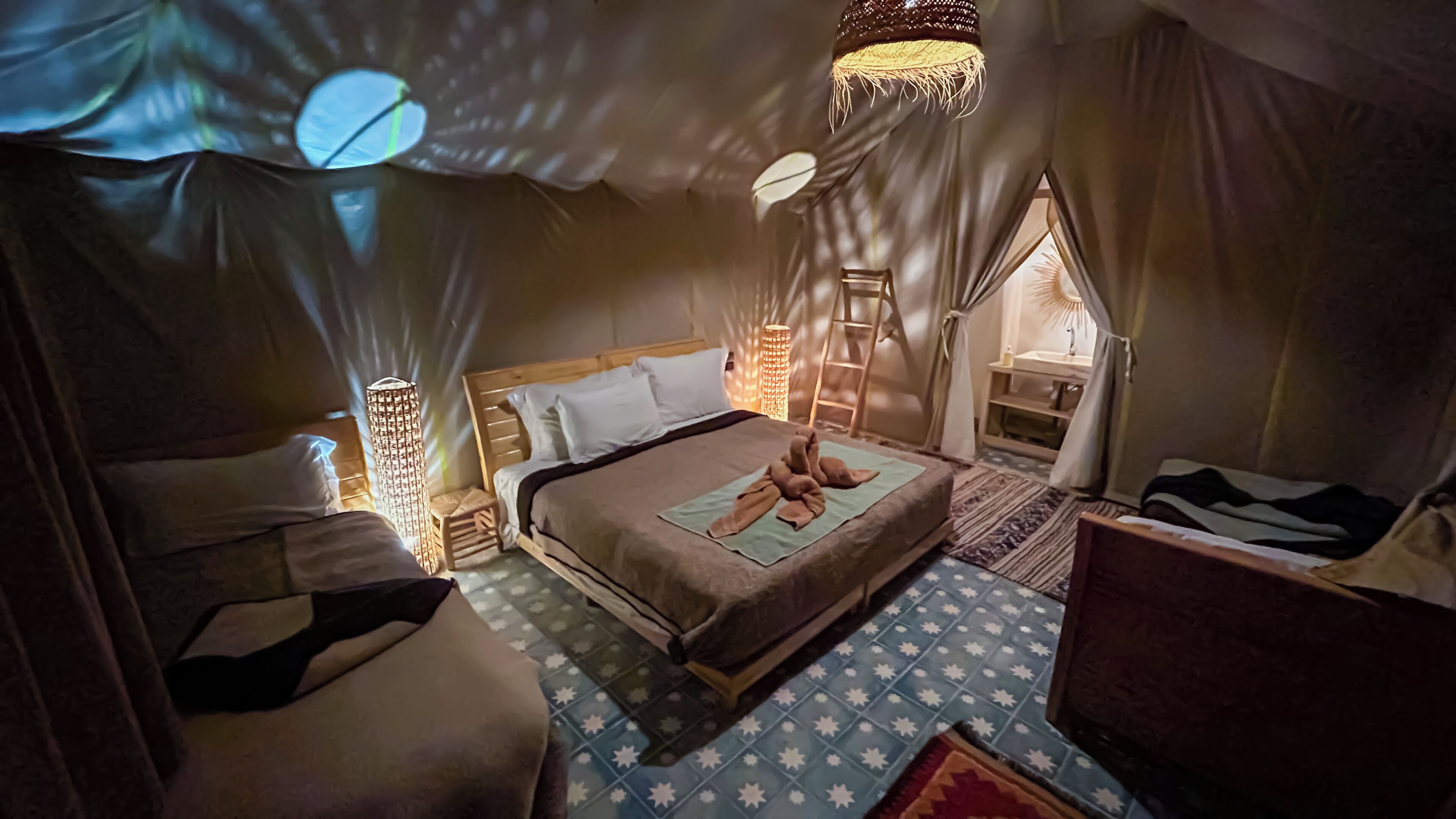 A cozy bedroom with a bed, bedside tables, a nightstand, a hanging light fixture, and a small window.