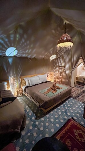 Une chambre confortable et bien éclairée, avec un grand lit, un luminaire suspendu et une vue sur l’extérieur par une fenêtre.