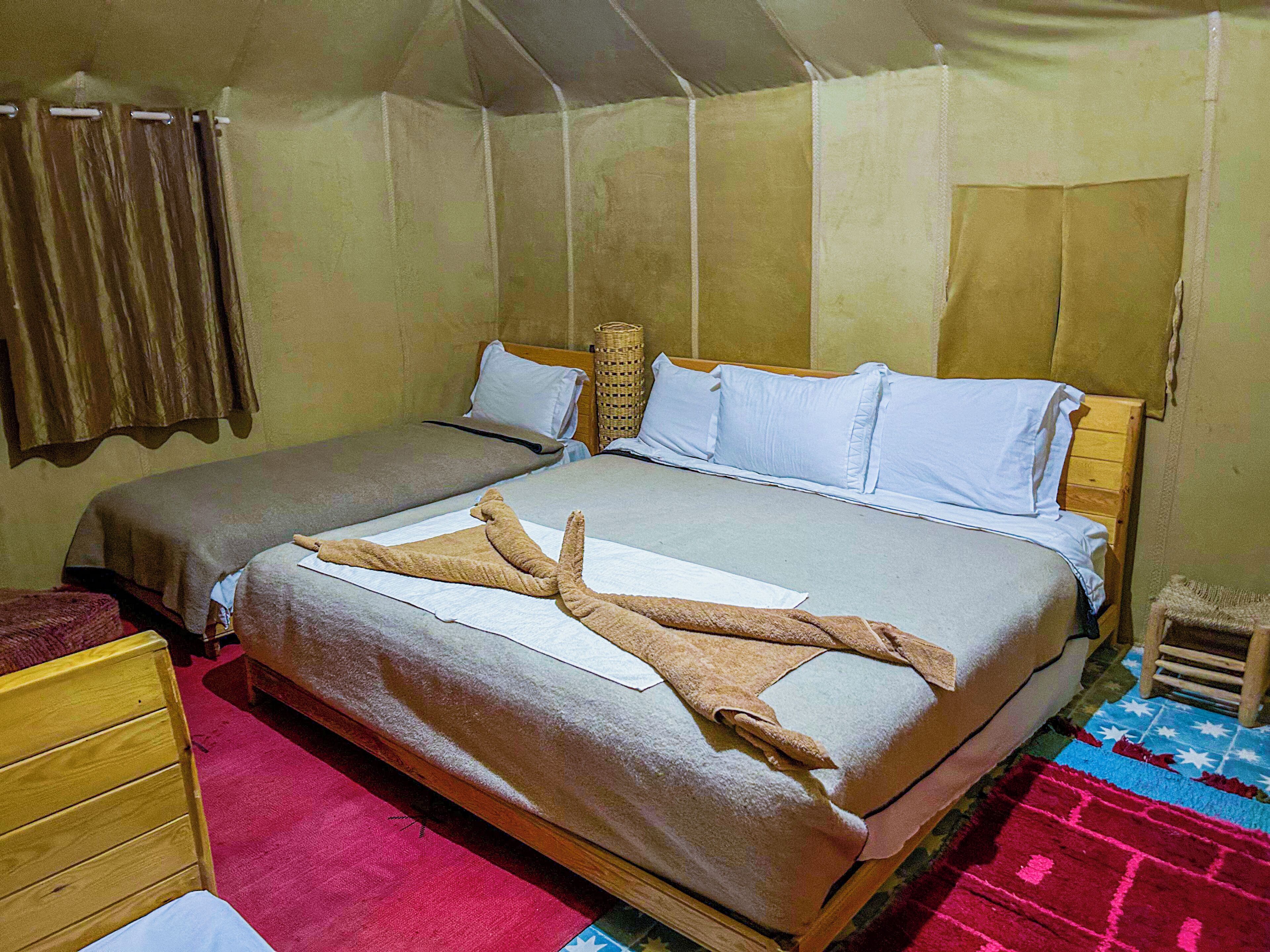 A tented accommodation with two beds, a wooden chair, and a red carpet.