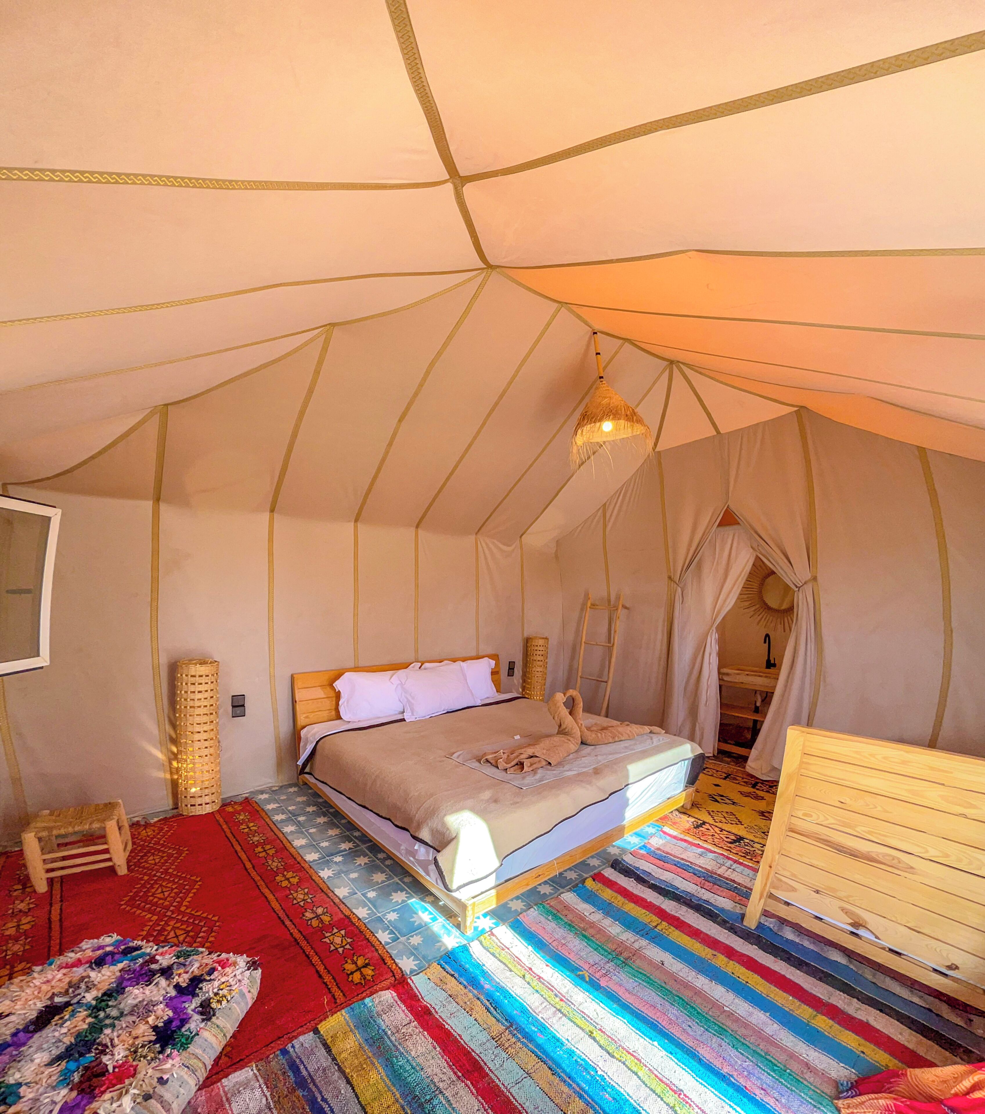Une pièce aménagée avec une tente, un lit, une commode en bois, un tapis coloré et un luminaire suspendu.