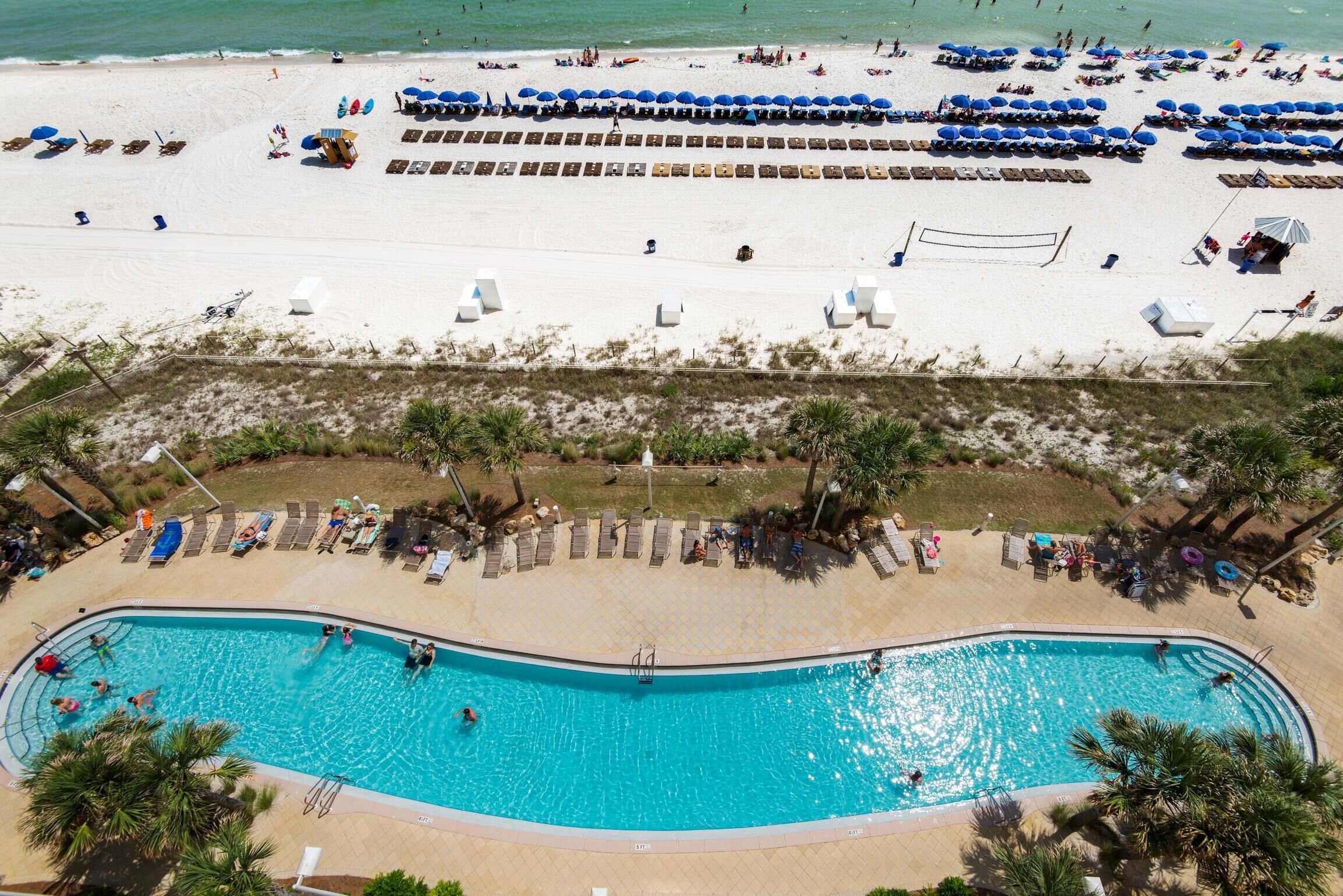 A beach with a swimming pool, sun loungers, and umbrellas.