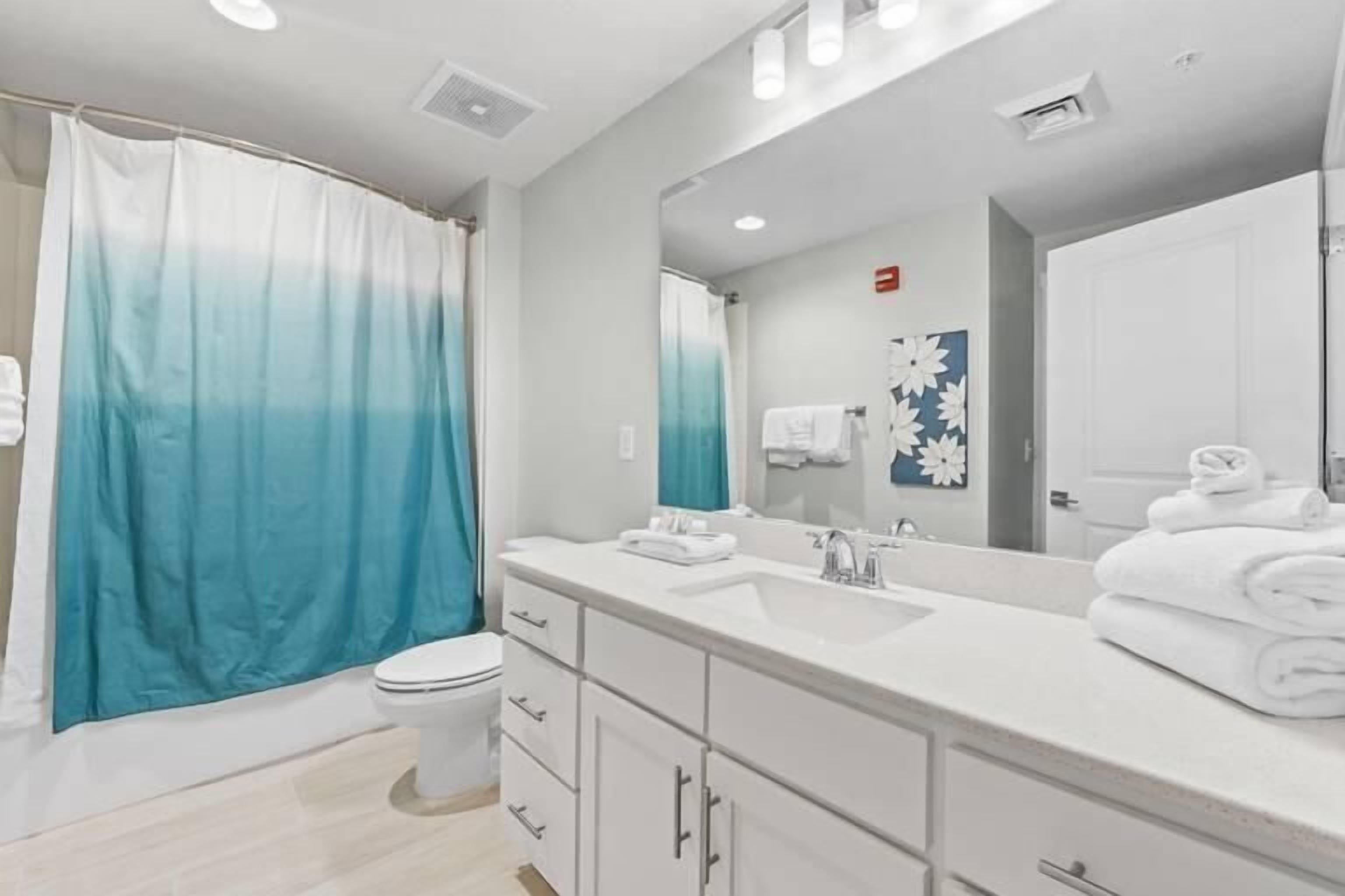 A modern bathroom with a shower curtain, toilet, sink, and mirror.