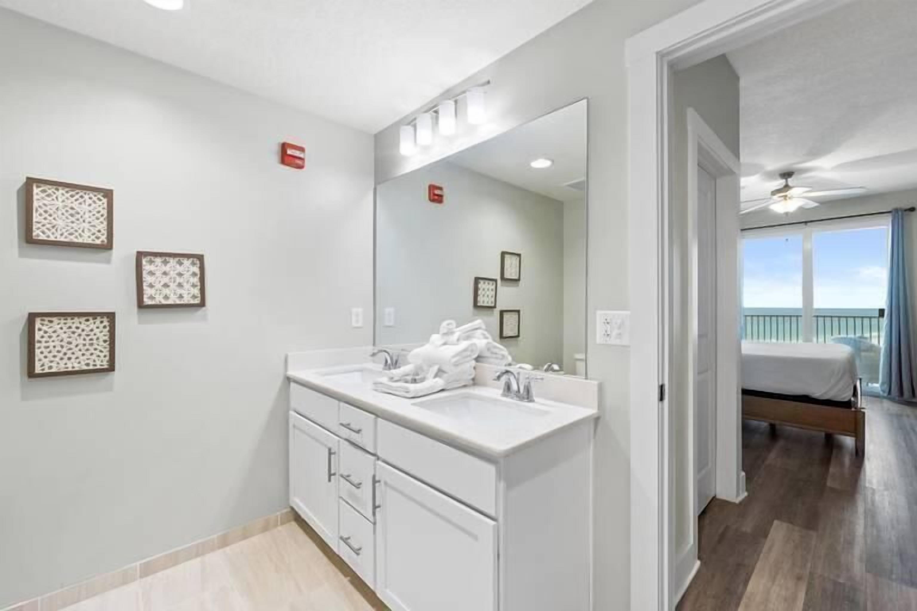 Een moderne badkamer met een grote spiegel, witte meubels en uitzicht op een balkon met een bed.