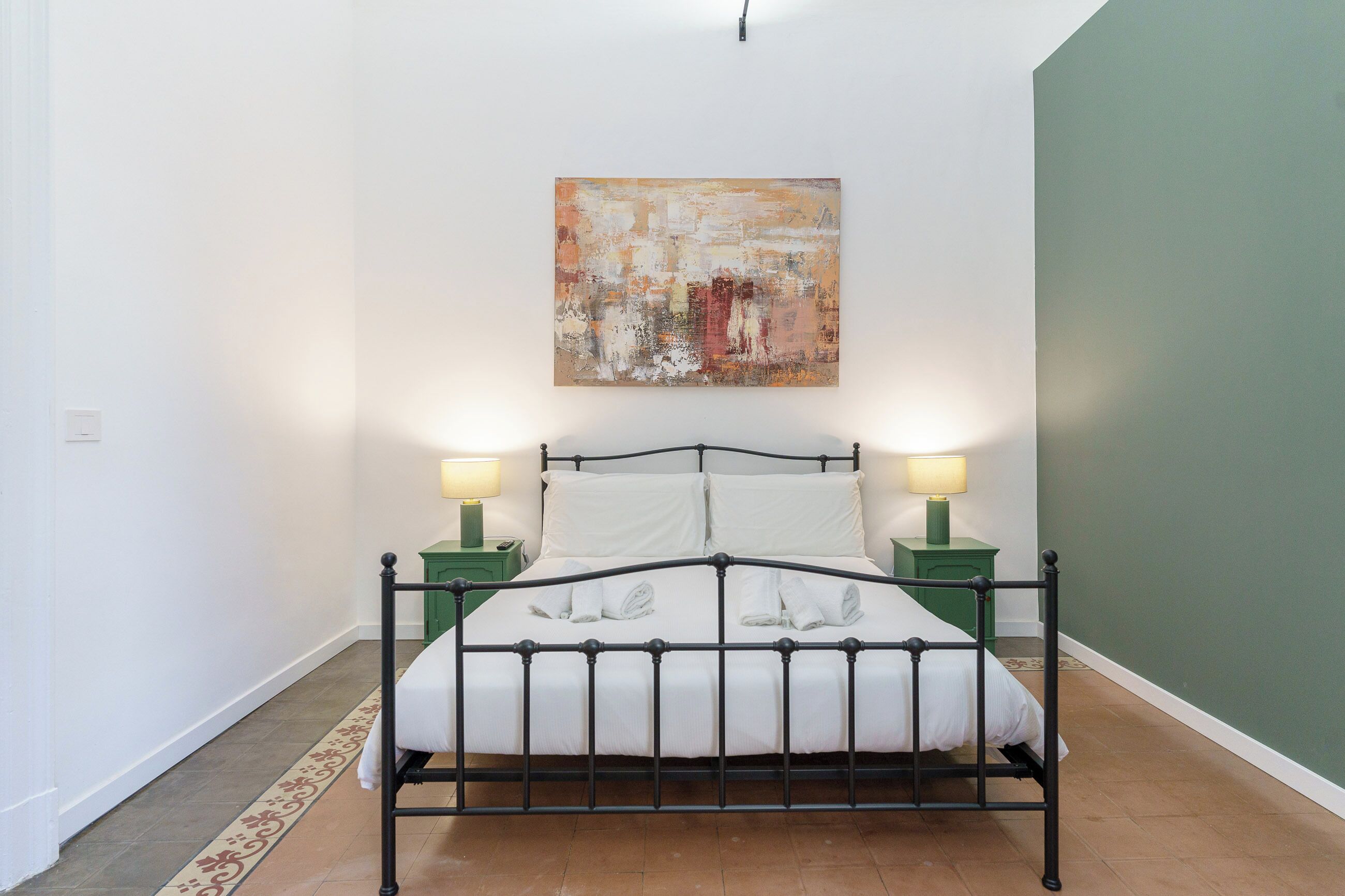 Un lit avec un cadre en métal, deux tables de chevet avec des lampes et un tableau au mur.
