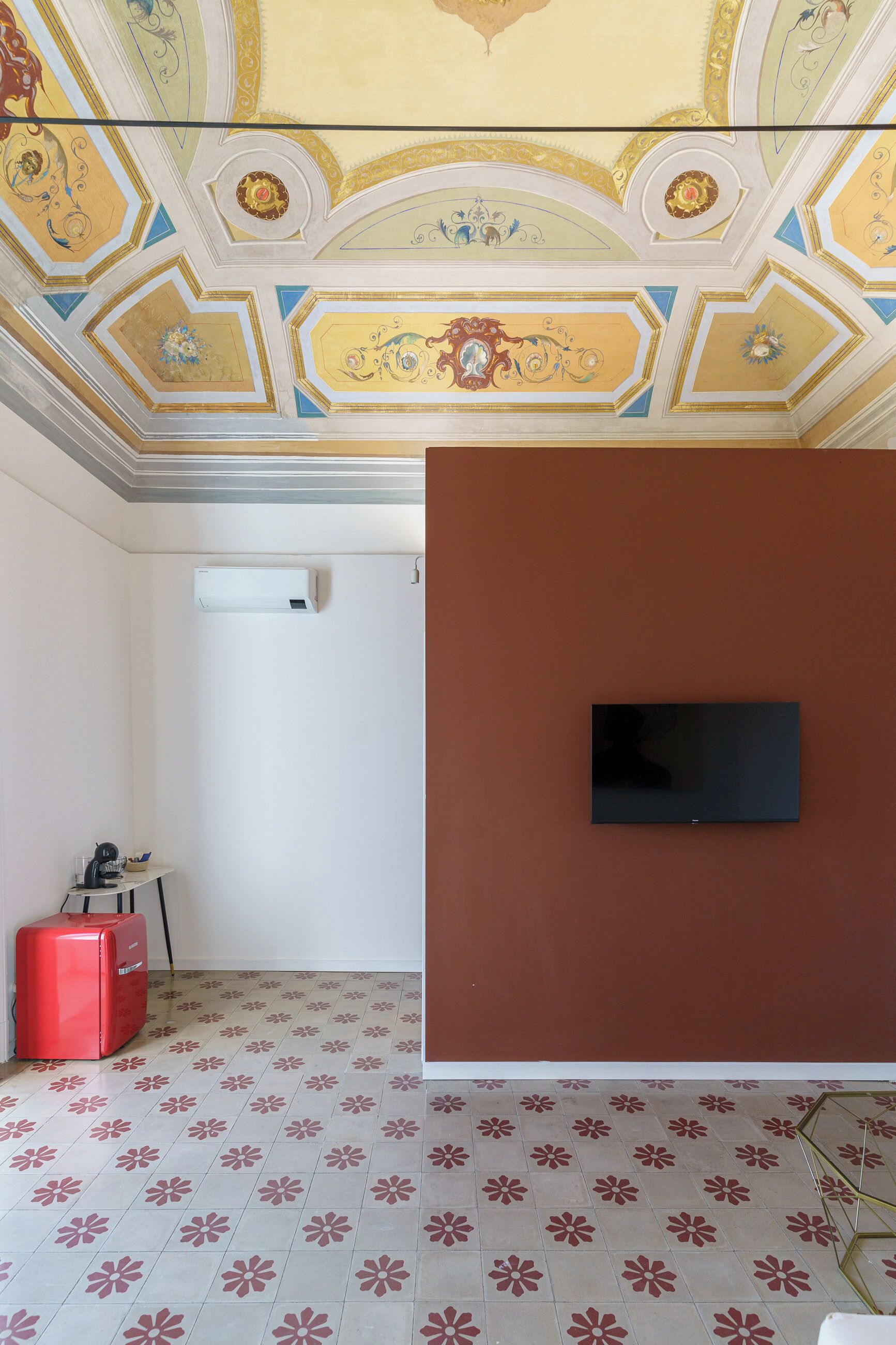 Ein Zimmer mit einem gemusterten Boden, einem an einer braunen Wand montierten Flachbildfernseher und einer Decke mit aufwendigen Verzierungen.