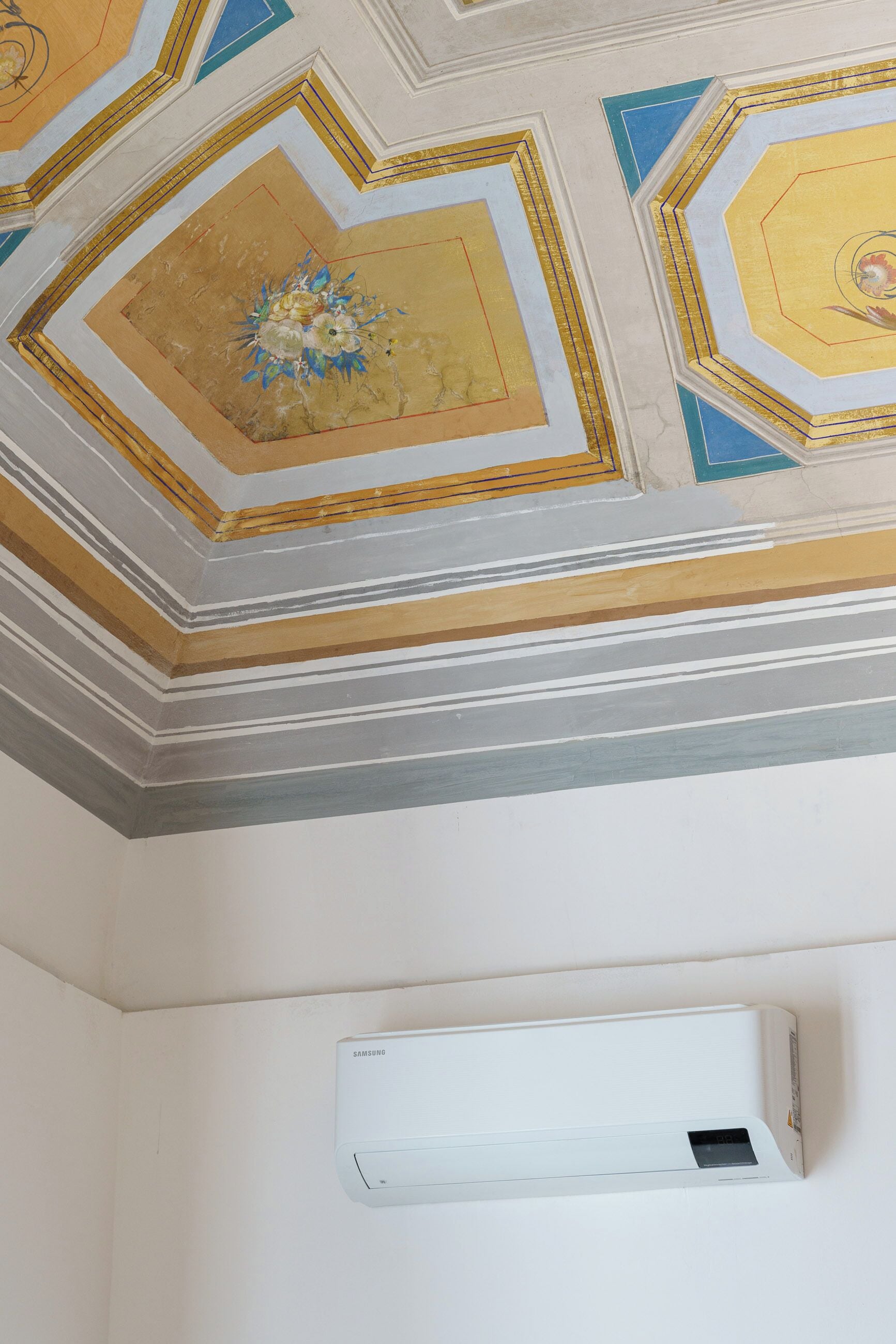 Una habitación con techo decorativo y unidad de aire acondicionado blanca.