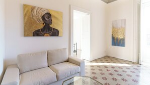 Un salon avec un canapé beige, une table basse en verre et deux tableaux accrochés au mur.