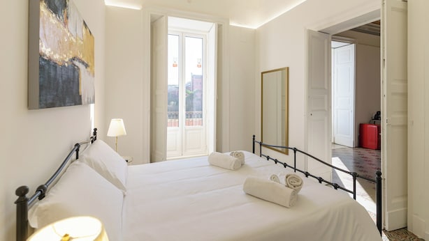 Une chambre d’hôtel avec un lit, une lampe de chevet, un grand tableau, un miroir et une vue sur le balcon extérieur.