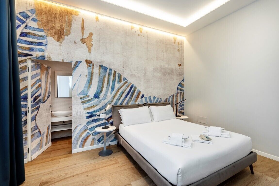 A modern bedroom with a large bed, a bedside table, a nightstand, and a wall with abstract art.