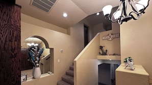 A hallway with a staircase, a decorative mirror, a vase with flowers, and a sign that reads "BEACH HOUSE".