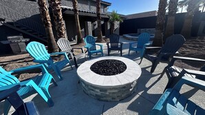 An outdoor seating area with Adirondack chairs and a stone fire pit.