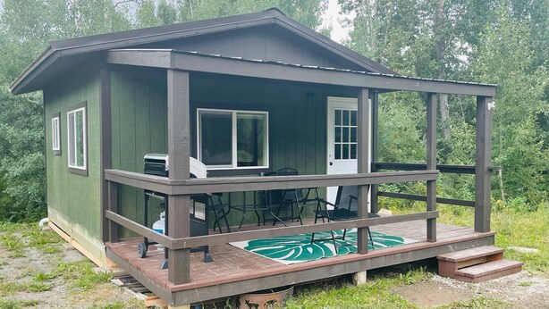 Une petite cabane avec une véranda, une table et des chaises.