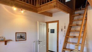 A bedroom with a wooden staircase, a bed, a door, and a small shelf with a picture.