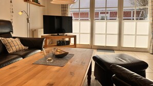 A living room with a wooden coffee table, black leather sofa, and a TV on a wooden stand.