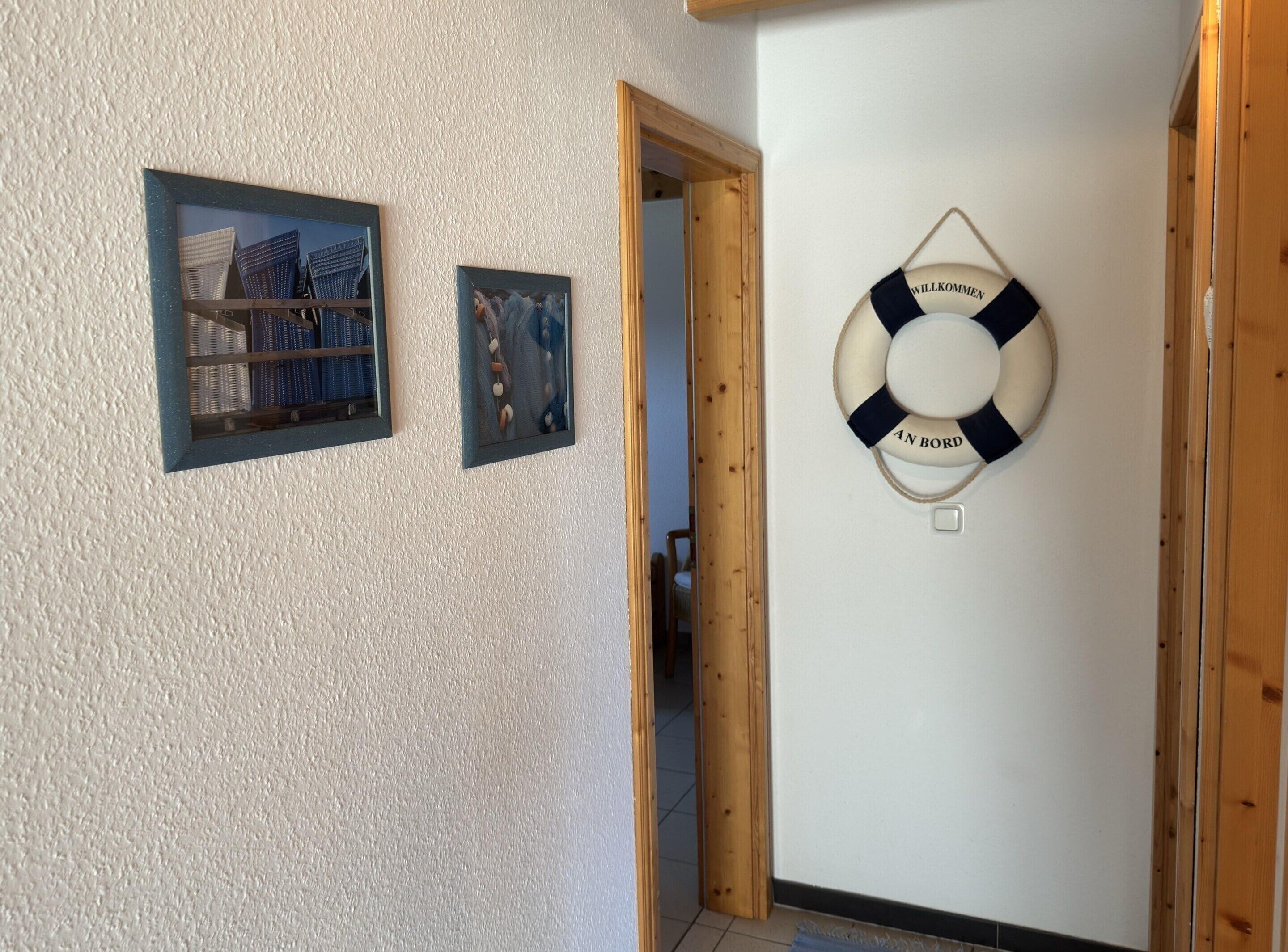 Ein Flur mit einem Rettungsflossen-Anhänger an der Wand, zwei gerahmten Bildern und einer Holztür.