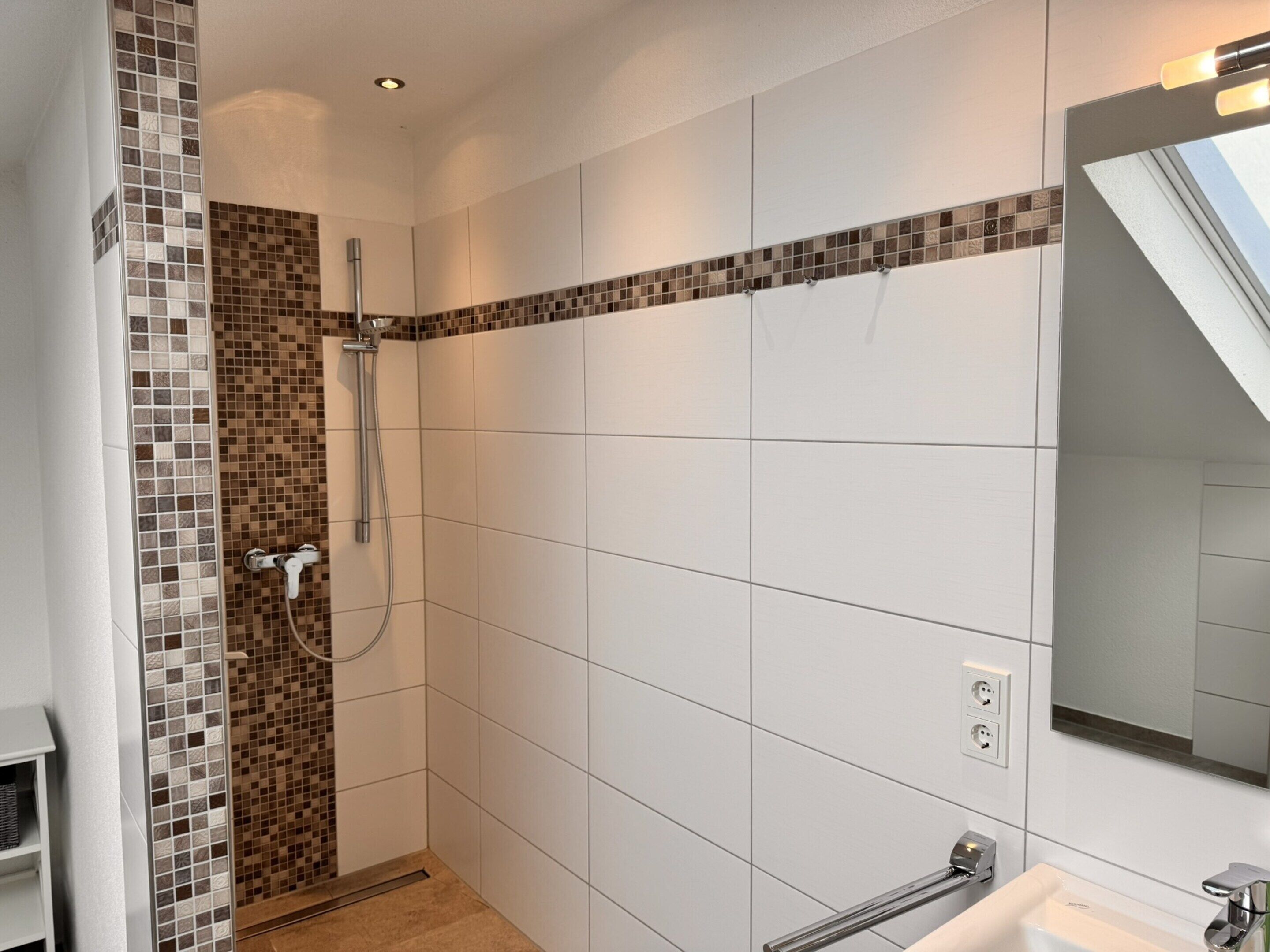 A modern bathroom with a shower, tiled walls, a sink, and a mirror.