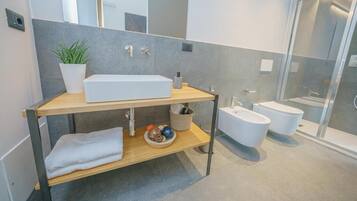 A modern bathroom with a large rectangular sink, a bidet, and a glass shower enclosure.